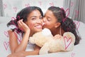 Composite image of pretty woman lying on bed with her daughter kissing cheek Royalty Free Stock Photo