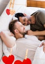 Composite image of red hanging heart and homosexual couple lying on bed