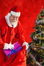 Composite image of santa claus putting presents in bag by christmas tree Royalty Free Stock Photo