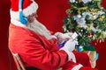 Composite image of santa claus using mobile phone with christmas tree Royalty Free Stock Photo