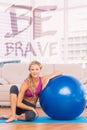 A Composite image of slim blonde sitting beside exercise ball smiling at camera