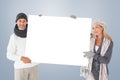 Composite image of smiling couple in winter fashion holding poster