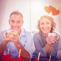 Composite image of smiling middle aged couple sitting on the couch having coffee Royalty Free Stock Photo