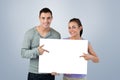 Composite image of smiling young couple pointing at sign they are holding Royalty Free Stock Photo