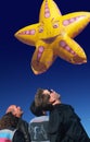 Composite image of spectators looking up at a scary yellow star-shaped balloon in the dark blue sky