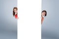 Composite image of teenage girls hiding behind a blank poster while showing their head from each sid Royalty Free Stock Photo