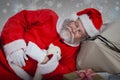 Composite image of tired santa claus sleeping beside christmas presents