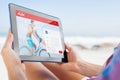 Composite image of woman sitting on beach in deck chair using tablet pc Royalty Free Stock Photo