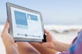 Composite image of woman sitting on beach in deck chair using tablet pc Royalty Free Stock Photo