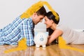 Composite image of young couple lying on floor smiling with piggy bank Royalty Free Stock Photo
