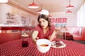 Composite image with young woman, waitress in 70s, 80s retro fashion style uniform sitting at table drinking coffee with Royalty Free Stock Photo