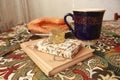 Composition of banana puff on a plate, a blue cup of tea, a fork, two notebooks and a citrine stone on a multi-colored tablecloth. Royalty Free Stock Photo
