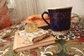 Composition of banana puff on a plate, a blue cup of tea, a fork, two notebooks and a citrine stone on a multi-colored tablecloth. Royalty Free Stock Photo