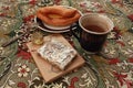 Composition of banana puff on a plate, a blue cup of tea, a fork, two notebooks and a citrine stone on a multi-colored tablecloth. Royalty Free Stock Photo