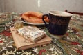 Composition of banana puff on a plate, a blue cup of tea, a fork, two notebooks and a citrine stone on a multi-colored tablecloth. Royalty Free Stock Photo