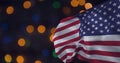 Composition of billowing american flag over orange, blue and green bokeh lights on dark background Royalty Free Stock Photo