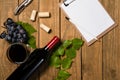 Composition with bottle and glass of wine with grape bunch and vine leaves and notepad on wooden background. Top view with copy