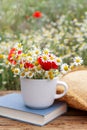 Composition with chamomiles, poppies, straw hat and book on table outdoors