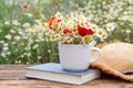 Composition with chamomiles, poppies, straw hat and book on table outdoors