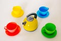 Composition from a children`s plastic set, consisting of four multi-colored tea cups with saucers and a yellow teapot in the cente Royalty Free Stock Photo