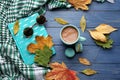 Composition with cup of aromatic coffee, warm plaid, book and autumn leaves on color wooden background