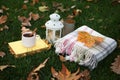 Composition with cup of coffee, book, plaid and autumn leaves on green grass outdoors