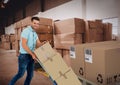 Composition of delivery man with trolley full of cardboard boxes, warehouse in background