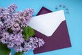 Composition with empty purple envelope and beautiful spring lilac flowers on blue background. Mockup card invitation Royalty Free Stock Photo