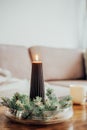 Composition of flaming black christmas taper candle placed between spruce branches on the coffee table in living room