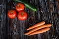 Composition of fresh vegetables on a wooden dark textured table. Carrots, tomatoes and ripe cucumber