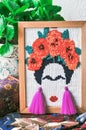 Composition from Frida Kahlo embroidery in a frame, a green plant in a pot, a wooden chest, golden leaves and velvety fabric in fl