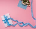 Composition of gift box with a long blue ribbon, a bouquet of flowers and an envelope on a pink background. Flat lay Royalty Free Stock Photo