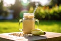 composition of glass jar with banana and oatmeal smoothie on the wooden table. outside sunny view with green grass background,