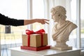 Composition with gypsum bust and hand. A box with a red ribbon in head and on the podium. Gift concept Royalty Free Stock Photo