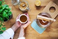 A composition of hands holding cup of tea, teapot and sugar on wooden table. A top view. Royalty Free Stock Photo