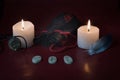 A composition of lighted candles, a bag of runes, an amulet with the image of Yggdrasil and a blue feather on a red background.