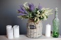 Composition of lilac and white flowers in a wicker vase and candles and a green bottle