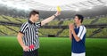 Composition of male referee holding yellow card and player at football stadium