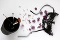 Composition of a masquerade black mask, spring flowers and tassels in a glass on a white background.