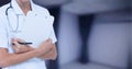 Composition of midsection of female doctor in lab coat holding clipboard over out of focus hospital