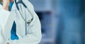 Composition of midsection of female doctor in lab coat with stethoscope over out of focus hospital