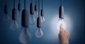 Composition of multiple light bulbs hanging with finger touching lit light bulb on blue background