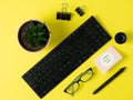 Composition of objects on a bright yellow background. Keyboard, glasses, a paper clip, graphic, pen, house plant, a card