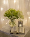 Composition: an open Bible, a bouquet of wildflowers in a vase and a decorative flashlight with a candle on the nightstand against