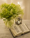 Composition: an open Bible, a bouquet of wildflowers in a vase and a decorative flashlight with a candle on the nightstand against