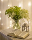 Composition: an open Bible, a bouquet of wildflowers in a vase and a decorative flashlight with a candle on the nightstand against