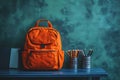 Orange Backpack with Pencils and Books on Blue Table Against Textured Teal Background Royalty Free Stock Photo