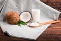 A composition of organic and bright brown coconuts, wooden spoon with grated nuts and coconut milk on a dark brown wooden table.