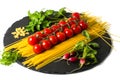 Composition of pasta fresh tomato, pepper, , radish on black stone board, white background. Royalty Free Stock Photo