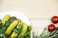 Composition with pickled cucumbers on the white plate with tomatoes, rosemary and parsley on wooden background. Cooking food